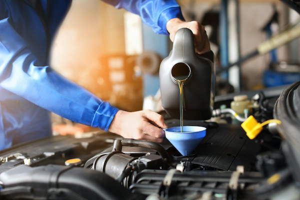 An automotive technician refilling oil with a funnel